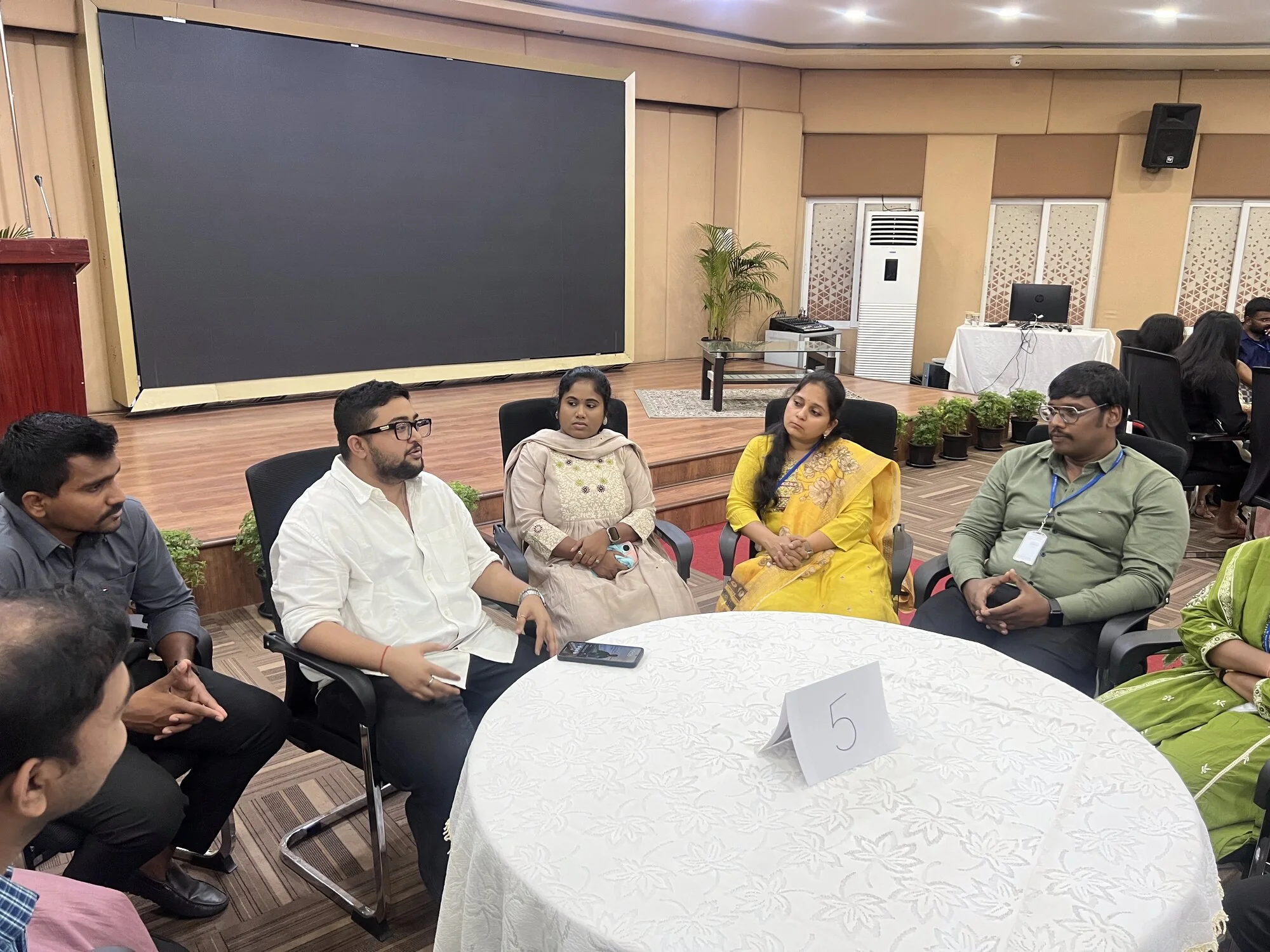 Five participants exchange ideas around a table during a conference session.